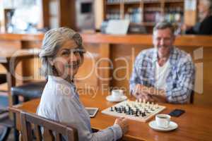 Man and woman looking at camera while playing chess