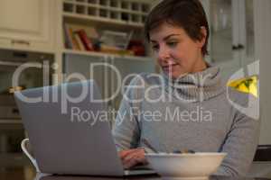 Woman having breakfast while using laptop