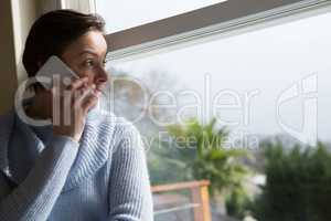 Woman talking on mobile phone near window