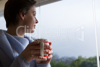 Woman looking through window while having coffee