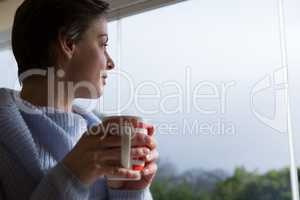 Woman looking through window while having coffee