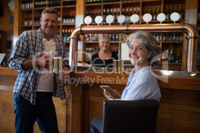 Happy man having beer and woman using digital tablet at counter