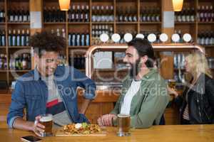 Two male friends having glass of beer and mexican food in bar