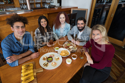 Friends sitting together with baby corn, snacks and beer on table in bar