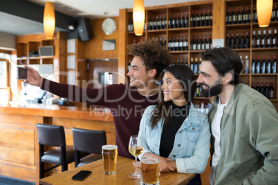 Friends taking selfie with mobile phone while having glass of beer