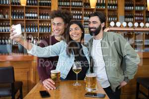 Friends taking selfie with mobile phone while having glass of beer