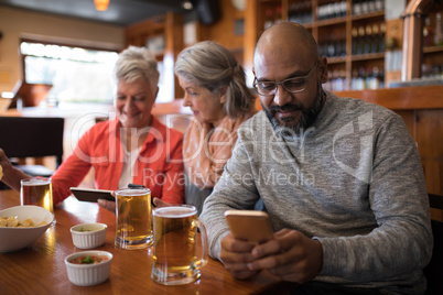 Senior friends using mobile phone in bar