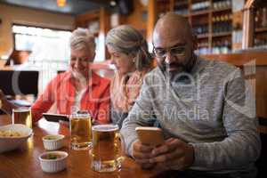 Senior friends using mobile phone in bar
