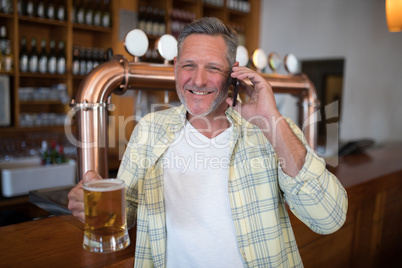 Smiling senior man talking on mobile phone while having glass of beer