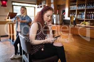 Beautiful woman sitting on chair and using mobile phone at counter