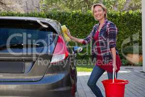 Smiling woman cleaning her car with sponge