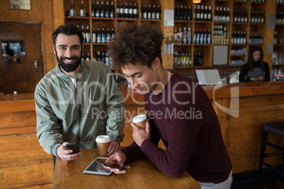 Two male friends using mobile phone while having coffee