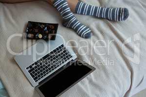 Low section of woman relaxing with chocolates and laptop on bed
