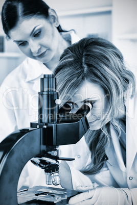 Young scientist looking through a microscope with her assistant