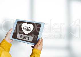 Hands holding tablet with Donate button and heart and money icon for charity