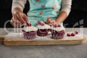 Woman arranging raspberries on cupcakes