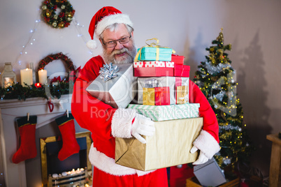 Santa claus holding a stack of gifts at home