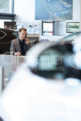 Car salesperson talking on landline phone in car showroom