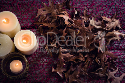 Lit candles and dry leaves on table