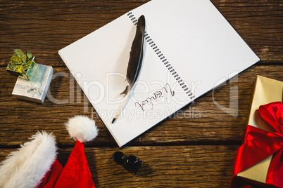 Wrapped gift, santa hat, diary and quill pen on wooden table in living room