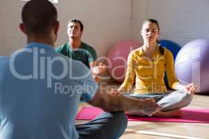 Instructor guiding students in meditation at health club