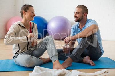 Instructor and student talking while having water in yoga studio