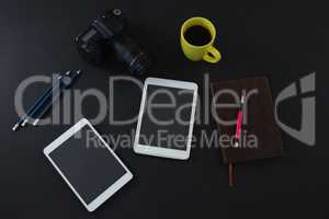 Digital tablet, black coffee, camera, organizer and pen on black background