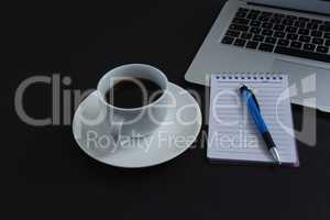 Black coffee, pen, notepad and laptop on black background