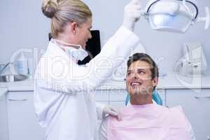 Dentist adjusting electric light while patient sitting on chair at clinic