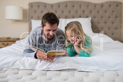 Father and daughter reading a book while lying on bed