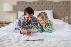 Father and daughter reading a book while lying on bed