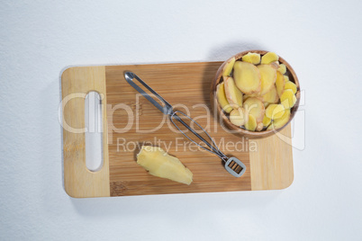 Overhead view of peeler and fresh ginger on wooden cutting board