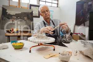 Attentive senior man molding clay