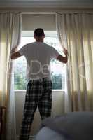 Man opening window curtain in bedroom