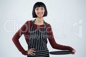 Smiling waitress holding empty tray against white background