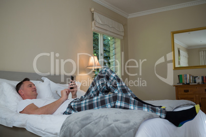 Man using mobile phone on bed in bedroom