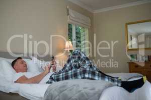 Man using mobile phone on bed in bedroom