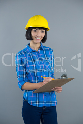 Female architect writing on clipboard against grey background