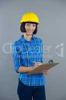 Female architect writing on clipboard against grey background