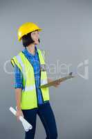 Female architect holding clipboard and blueprint against grey background