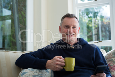 Man using mobile phone while having cup of coffee in living room