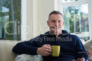 Man using mobile phone while having cup of coffee in living room