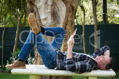 Man lying on bench and using digital tablet in garden