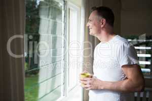 Man looking through window while having cup of coffee