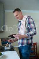 Man using digital tablet while preparing food in pan
