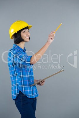 Female architect holding clipboard and gesturing against grey background