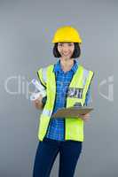 Female architect holding clipboard and blueprint against grey background