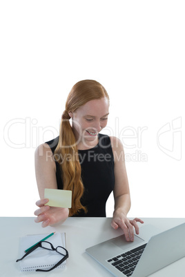 Female executive holding visiting card while using laptop