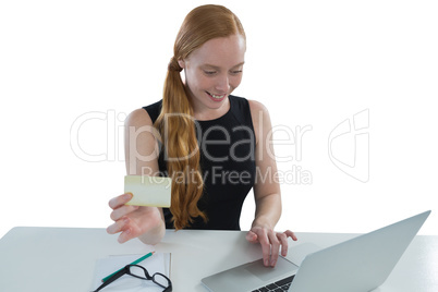 Female executive holding visiting card while using laptop