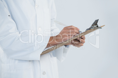 Doctor writing on clipboard against white background